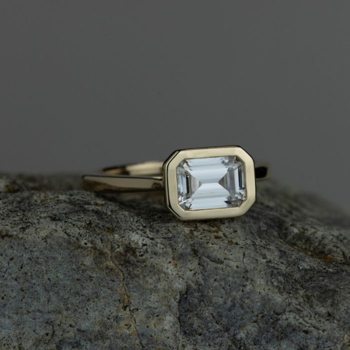 The-Adeline-Bezel-Set-Emerald-Cut-Moissanite-Engagement-Ring-on-a-rock