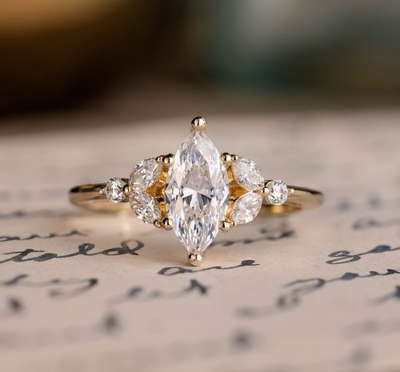 An engagement ring with a marquise-cut diamond center stone and smaller round diamonds on either side, resting on an old handwritten letter with a soft-focus background.