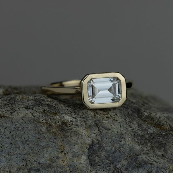 The-Adeline-Bezel-Set-Emerald-Cut-Moissanite-Engagement-Ring-on-a-rock