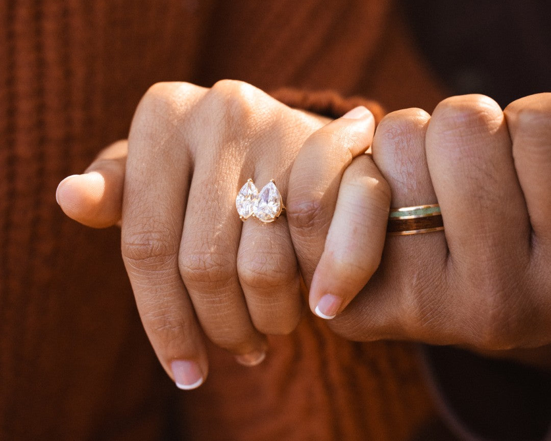 Close-up of two hands holding each other, one wearing a diamond ring and the other a gold band.