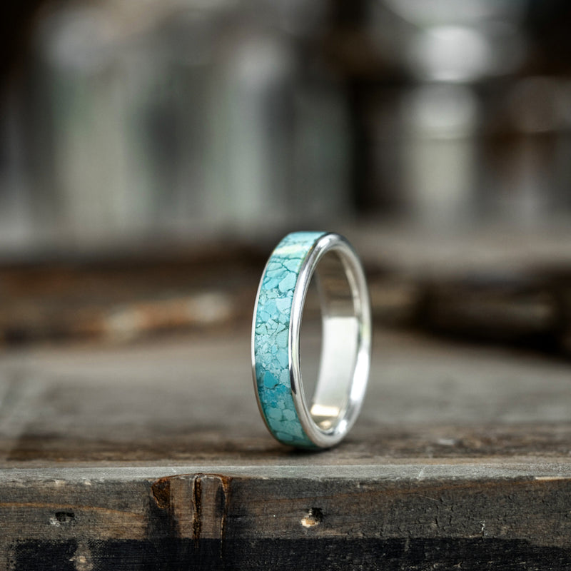 Silver ring with turquoise inlay on a wooden surface