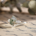Angled view of The Liora white gold ring featuring a pear-shaped moss agate center stone, pear-shaped diamond side stones, and smaller diamond accents set underneath.