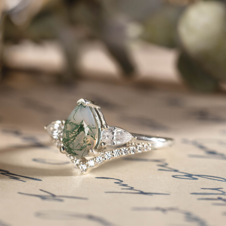 Angled view of The Liora white gold ring featuring a pear-shaped moss agate center stone, pear-shaped diamond side stones, and smaller diamond accents set underneath.