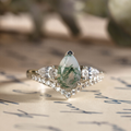 Front view of The Liora white gold ring featuring a pear-shaped moss agate center stone, two pear-shaped diamond side stones, and a row of smaller diamond accents underneath.