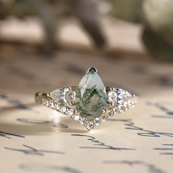 Front view of The Liora white gold ring featuring a pear-shaped moss agate center stone, two pear-shaped diamond side stones, and a row of smaller diamond accents underneath.