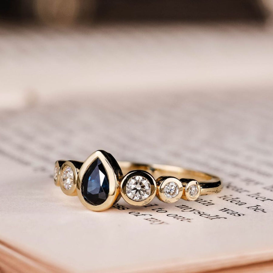 the-lyra-bezel-set-pear-cut-blue-sapphire-engagement-ring-diamond-accents