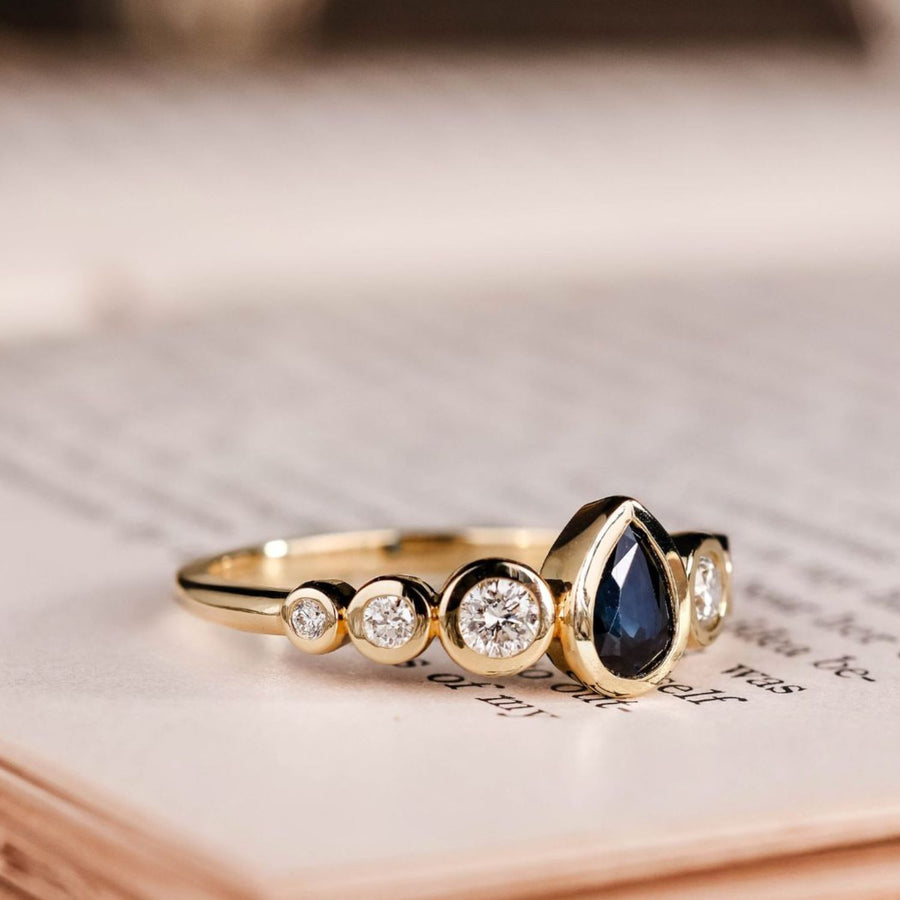 the-lyra-bezel-set-pear-cut-blue-sapphire-engagement-ring-diamond-accents