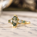 Angled front view of The Titania yellow gold ring featuring a marquise moss agate center stone with clear and green accent stones along the band.