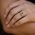 Close-up of The Titania yellow gold ring worn on hand, featuring a marquise moss agate center stone and sparkling clear and green accent stones along the band.