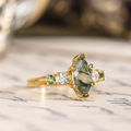 Three-quarter view of The Titania yellow gold ring showcasing a marquise moss agate center stone framed by sparkling clear and green accent stones.
