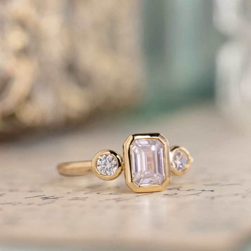three-stone-emerald-cut-diamond-engagement-ring-round-diamond-accents-bezel-setting-the-marcelline-rustic-and-main