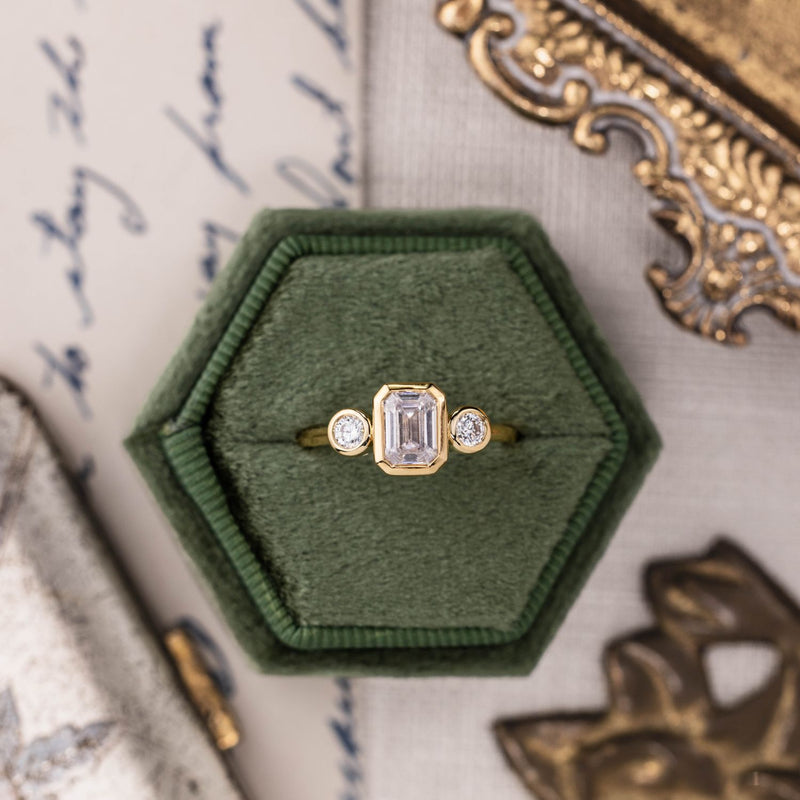 three-stone-emerald-cut-diamond-engagement-ring-round-diamond-accents-bezel-setting-the-marcelline-rustic-and-main