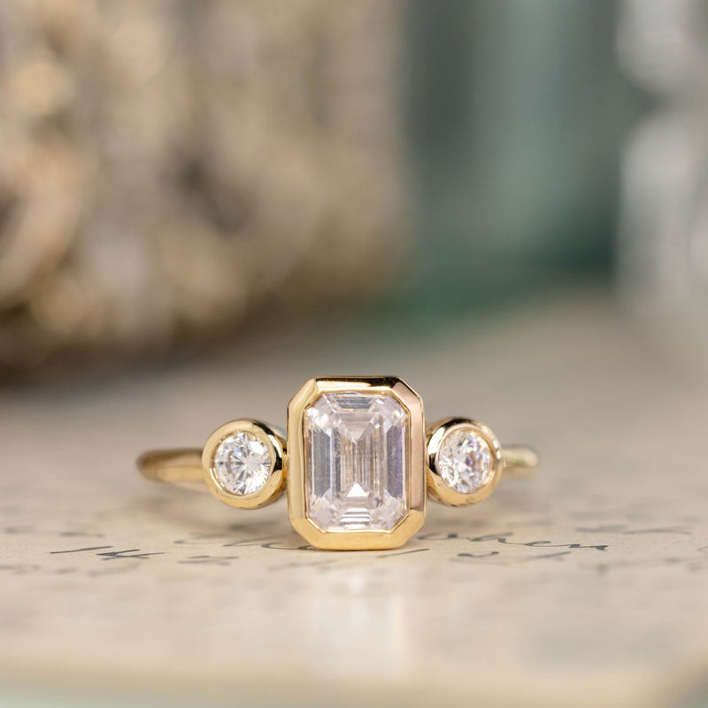 three-stone-emerald-cut-diamond-engagement-ring-round-diamond-accents-bezel-setting-the-marcelline-rustic-and-main